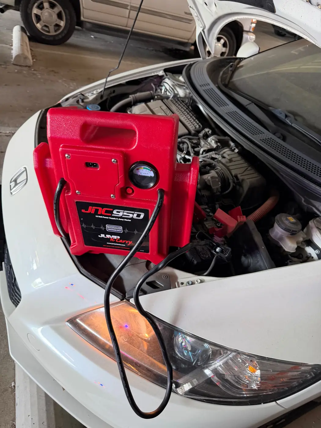 JNC950 jump pack clamped to a Honda sedan battery in a DFW garage during a 24/7 mobile jump start call.