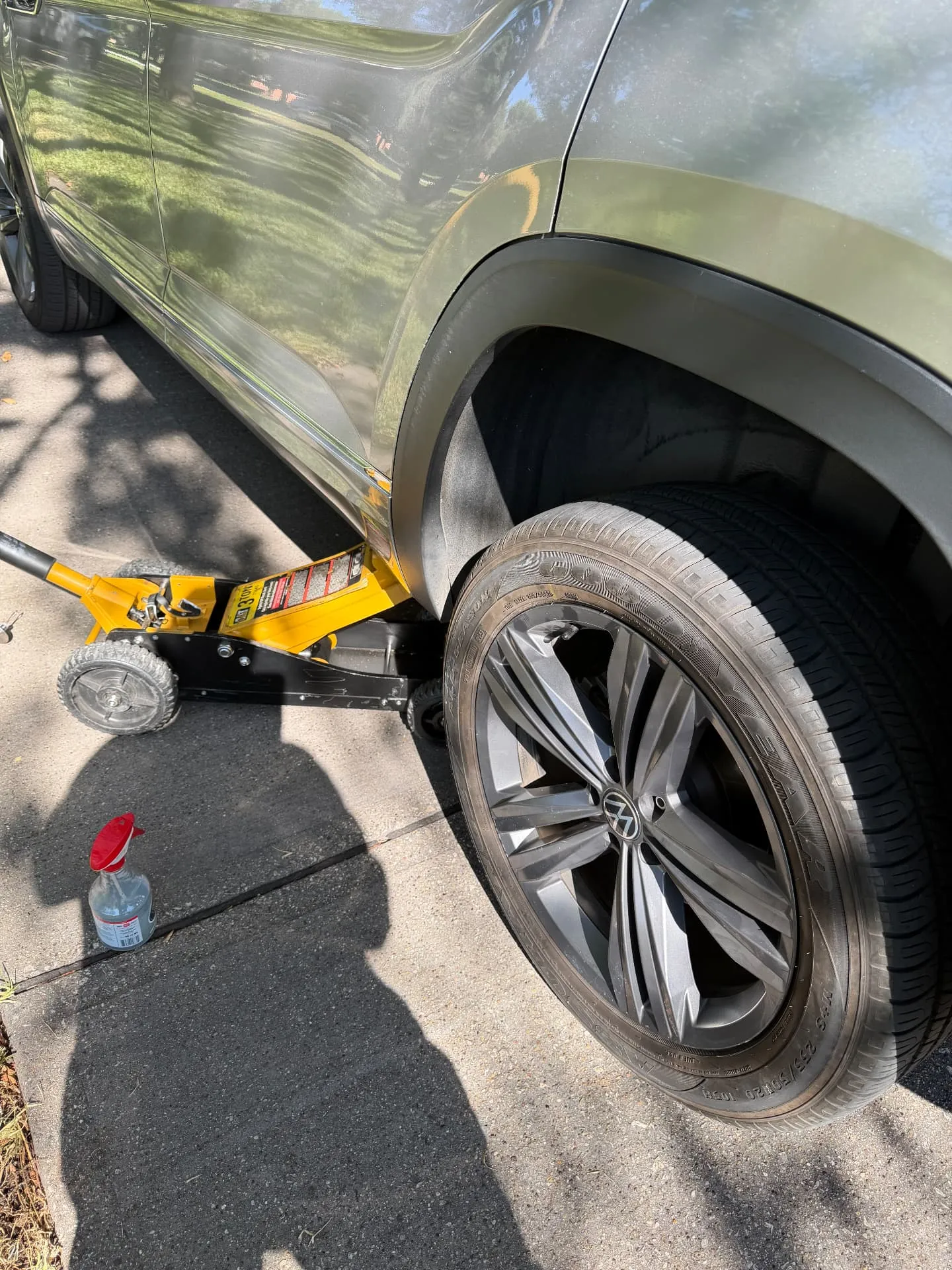 Green Volkswagen Atlas lifted on a yellow floor jack in a west Fort Worth driveway with the front wheel ready to come off during a mobile tire change in 76116.