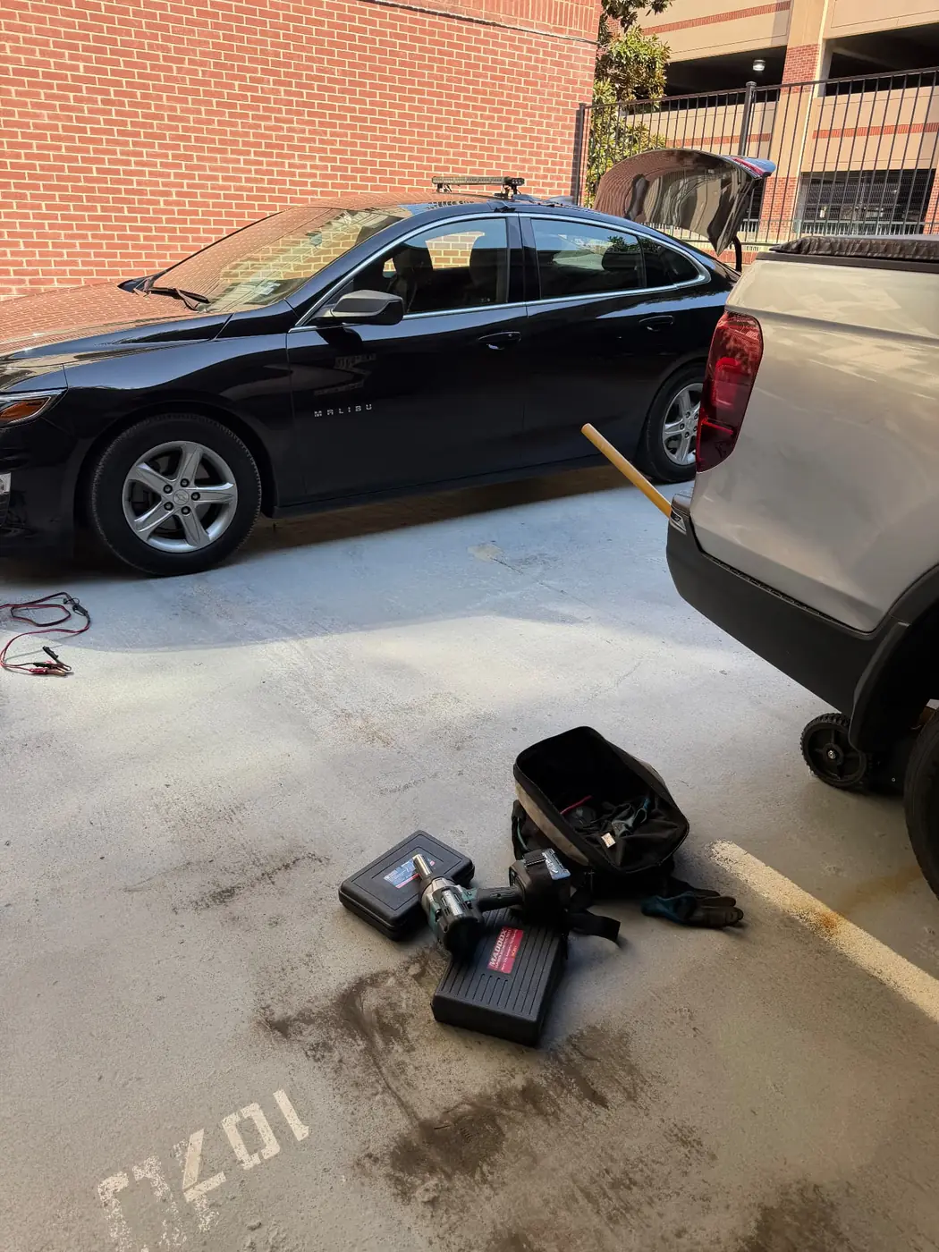 Chevrolet Malibu in a covered Dallas parking garage with the service truck backed in and an impact wrench staged for a mobile tire replacement.