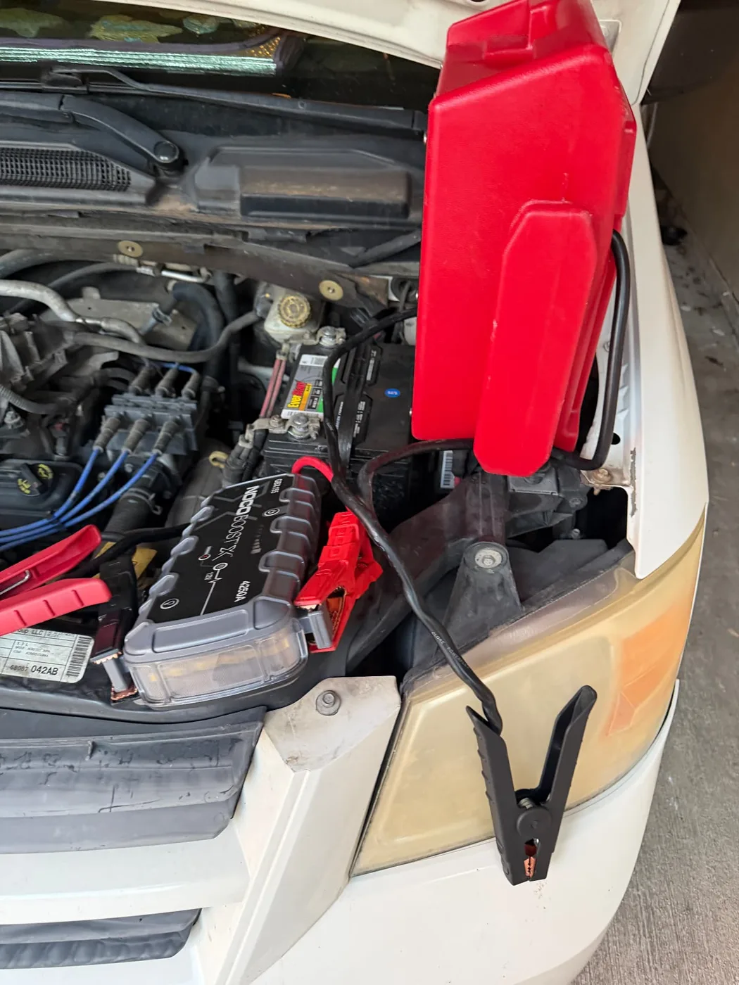NOCO Boost X GBX155 4250-amp jump pack and a red JNC950 booster clamped to the Everstart 12V battery of a white minivan in Arlington, Texas.