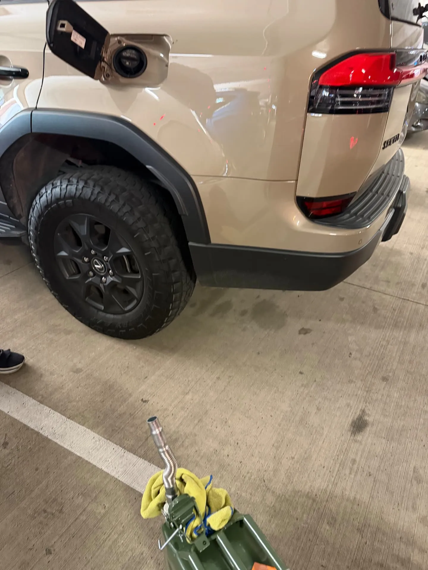 Tan Nissan SUV with its fuel door open in a covered downtown Fort Worth parking garage, steel fuel can and spout staged on the deck during an emergency mobile fuel delivery in 76102.