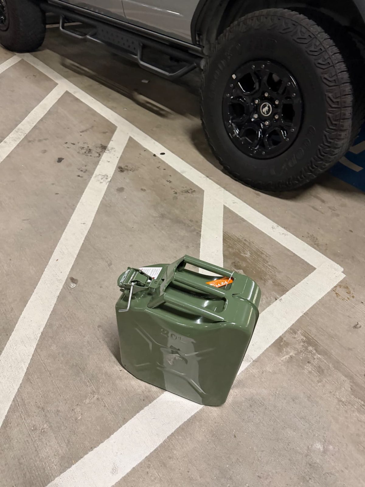 Green 20-liter steel fuel can staged on the concrete beside a Ford Bronco in a Dallas parking garage during an emergency mobile fuel delivery.