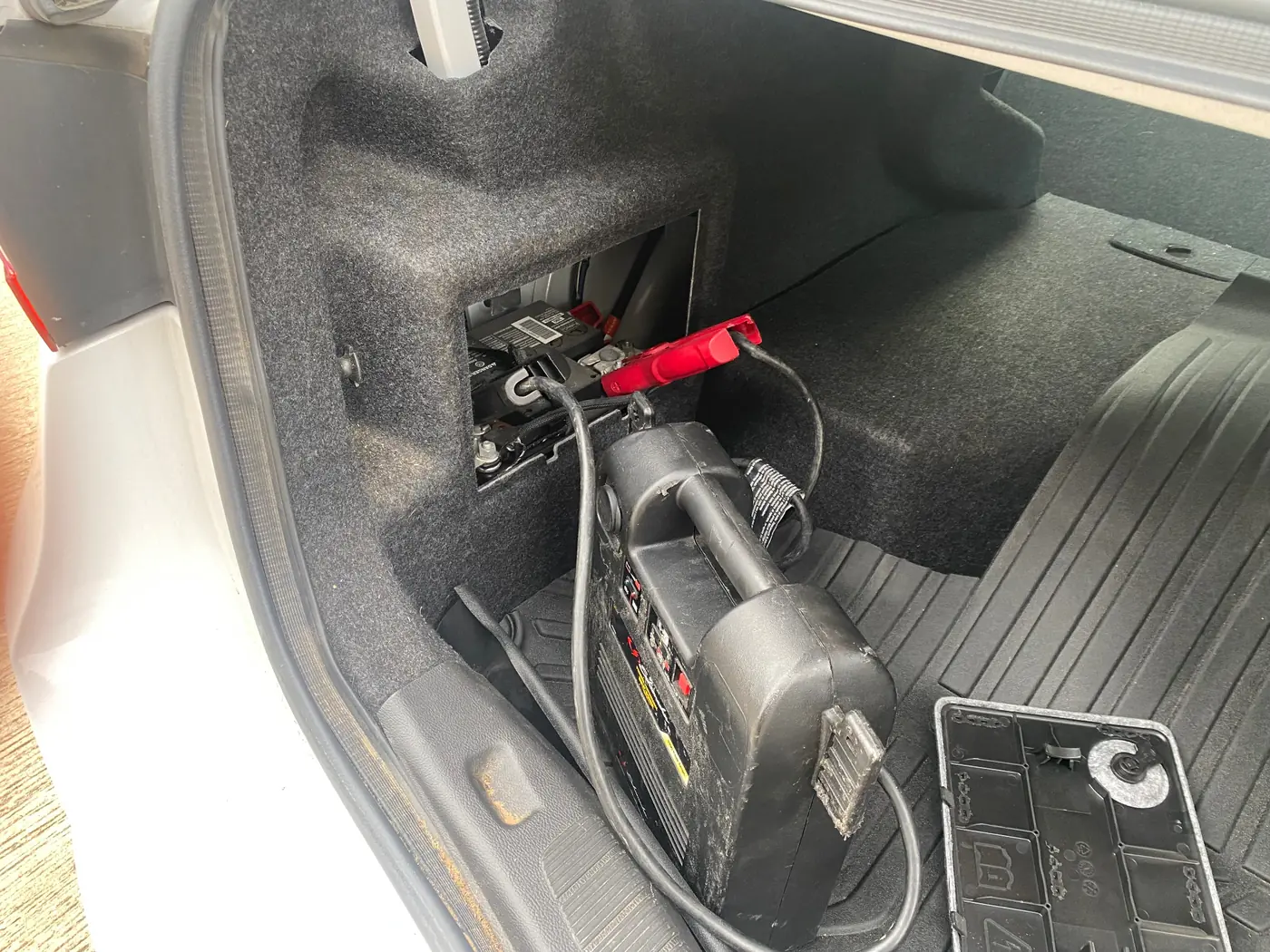 Technician connecting a jump pack to the trunk-mounted battery of a luxury European sedan in Dallas, Texas.