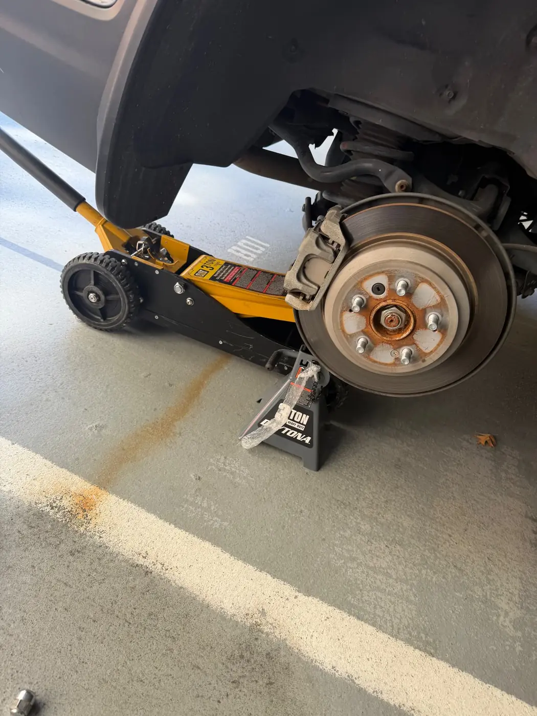 Wheel removed and vehicle supported on a floor jack during an on-site tire replacement in Dallas, Texas.