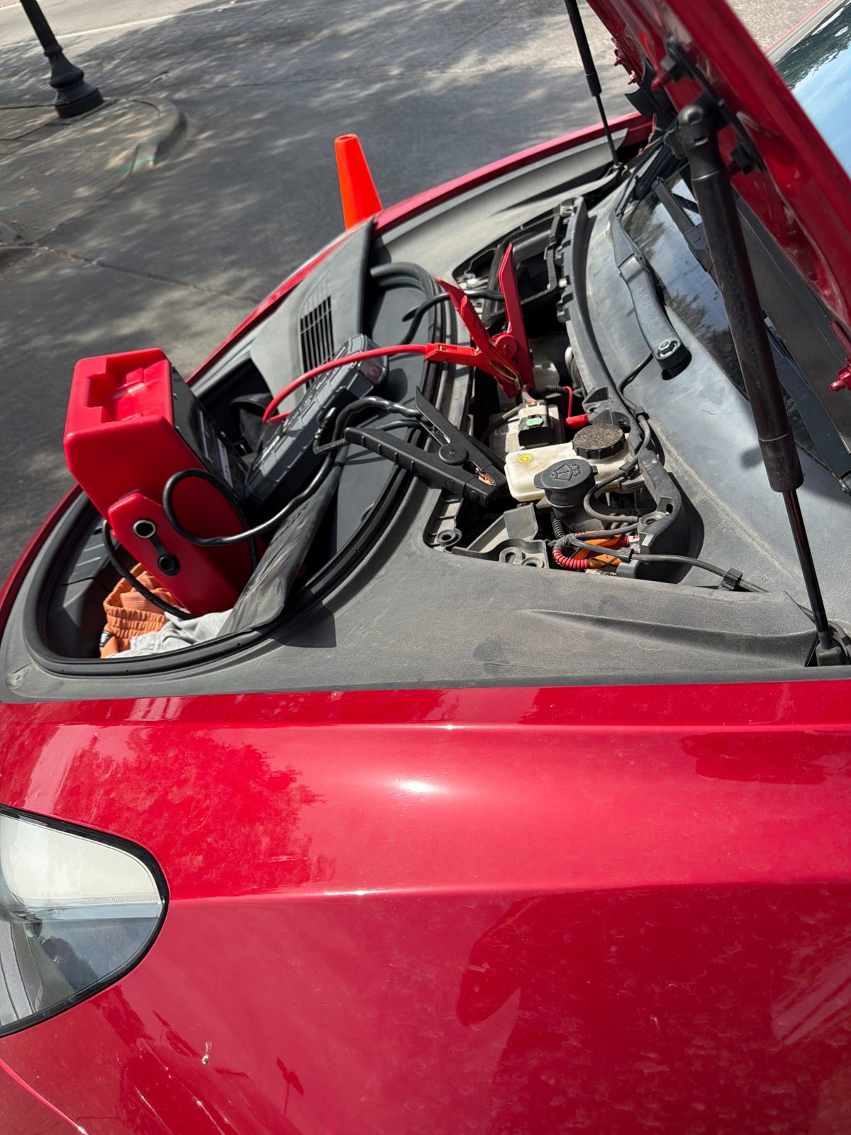 Jump pack clamped to the 12V battery in the frunk of a red Tesla Model 3 during a mobile Tesla 12V battery replacement in Dallas-Fort Worth