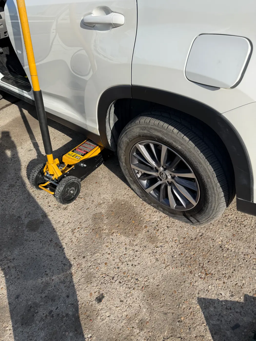 Toyota Highlander lifted on a floor jack during a mobile tire change on a Dallas-Fort Worth driveway, wheel off and lug nuts staged.